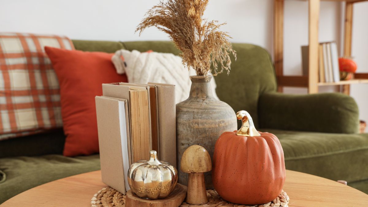 Őszi dekorációs elemek, mint például díszpárnák, könyvek és tökök egy asztalon.