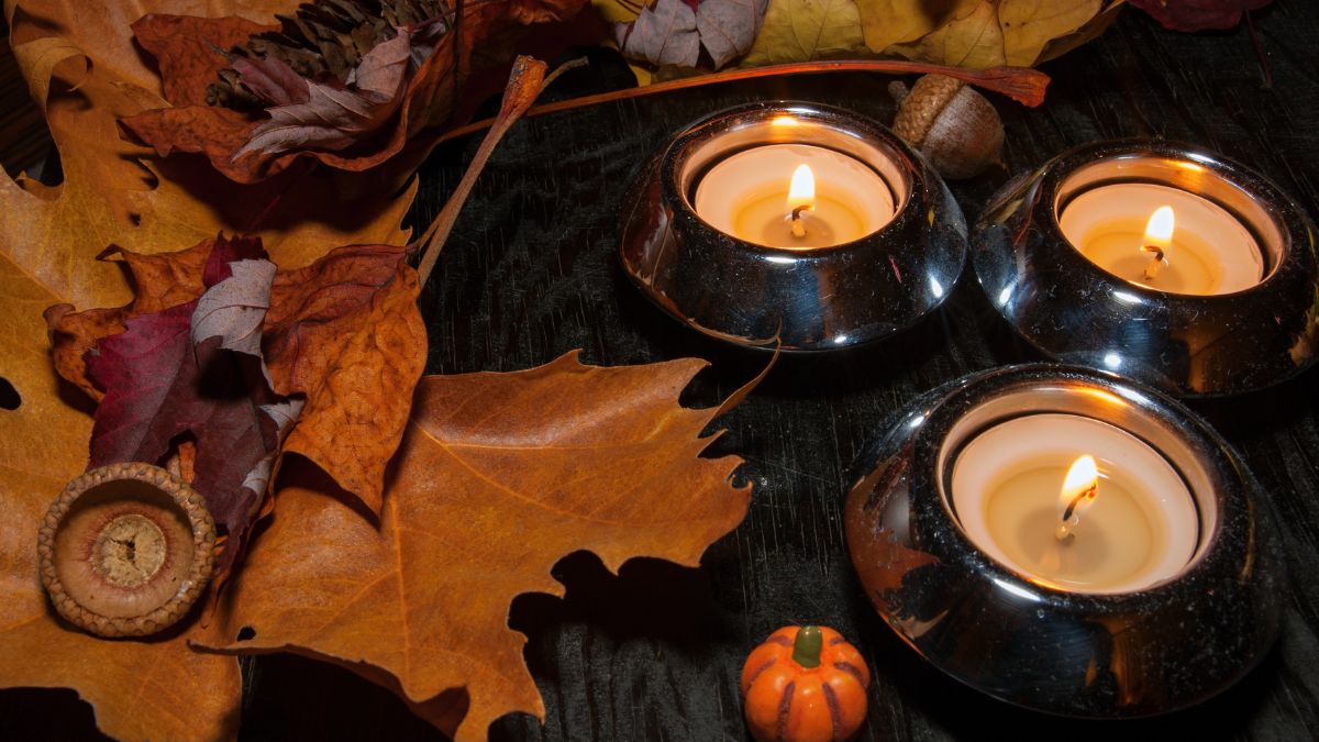 Három égő gyertya, színes őszi levelek és egy kis tök díszíti a sötét asztalt.
